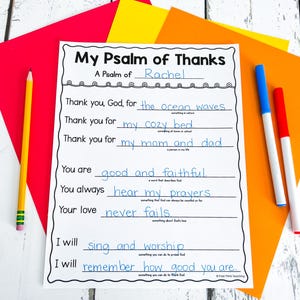 Op de afbeelding: Een wit, bedrukbaar werkblad met de titel "My Psalm of Thanks" met invullijnen. Het werkblad is omgeven door gekleurd papier en schrijfgerei, waaronder een gele potlood en blauwe en rode stiften.
