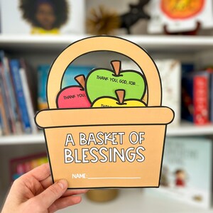 Op de afbeelding: Een bruine papieren manduitsparing met een handvat, gevuld met appeluitsparingen. De appels zijn rood, groen en geel met de tekst "Thank You, God, For..." en "Thank You." De mand heeft de tekst "A Basket of Blessings" en een ruimte voor een naam.