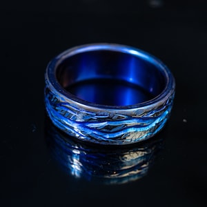 May include: A blue titanium ring with a textured, wave-like design. The ring is polished and has a high shine.