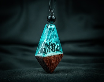 May include: A teal blue resin pendant with a wood base, featuring a swirling pattern inside. The pendant is attached to a black cord with a black bead.