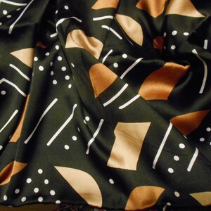 Puede incluir: Tela negra con un patr&oacute;n geom&eacute;trico de l&iacute;neas blancas y formas marrones. La tela est&aacute; doblada y tiene una textura suave y sedosa.