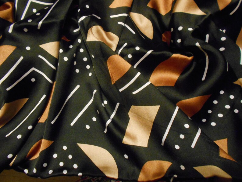 Puede incluir: Tela negra con un patr&oacute;n geom&eacute;trico de l&iacute;neas blancas y formas marrones. La tela est&aacute; arrugada y tiene un brillo satinado.