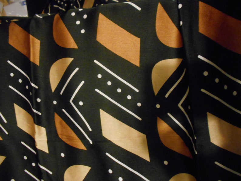 Puede incluir: Tela negra con un patr&oacute;n geom&eacute;trico de l&iacute;neas blancas, formas marrones y tostadas y puntos blancos.