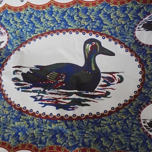 May include: A white fabric with a blue and green floral pattern. The fabric features a repeating design of a duck swimming in a pond, surrounded by a white oval with a red and white border.