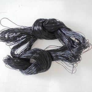 Op de afbeelding: Close-up van zwart koord geknoopt op twee plaatsen. Het koord is dun en lijkt gemaakt van een synthetisch materiaal. De achtergrond is effen wit.