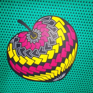 May include: A green fabric with a repeating pattern of black triangles. A large stylized apple with a black, yellow, and pink geometric design is centered on the fabric.