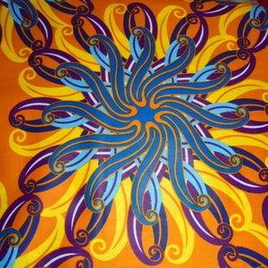 Op de afbeelding: Een levendige oranje stof met een herhalend patroon van blauwe, gele en paarse swirls. Het patroon is gecentreerd rond een groot, blauw, stervormig ontwerp.