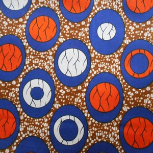May include: A brown fabric with a repeating pattern of blue, white, and orange circles. The circles have a white or orange center with a blue or orange ring around it.