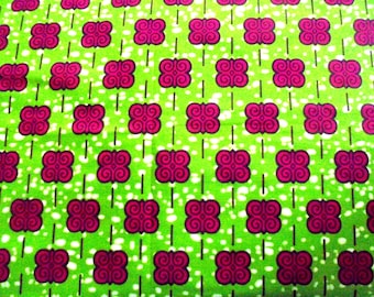 May include: Close-up of a vibrant fabric with a repeating pattern. The design features magenta-colored, stylized butterfly-like shapes set against a bright green background. Thin black lines and white dots add detail to the textile.