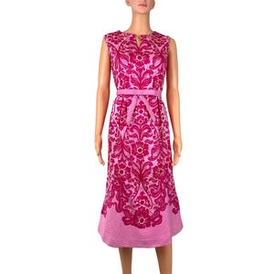 May include: A sleeveless midi dress featuring a vibrant magenta and light pink floral damask pattern. The dress includes a matching fabric belt at the waist, a small notch neckline, and a hemline finished with a subtle horizontal striped texture.