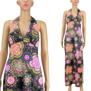 May include: A black halter-neck maxi dress with a vibrant floral pattern in pink, yellow, and purple. The dress features a V-neckline and a side slit, showcasing a retro, bohemian style.