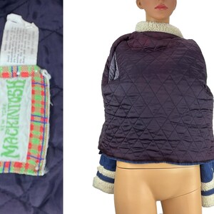 K&ouml;nnte beinhalten: Gesteppte marineblaue Jacke mit cremefarbenem Shearling-Kragen. Die Jacke hat blaue Jeans&auml;rmel mit cremefarbenen Streifen und eine cremefarbene Shearling-Manschette. Ein Etikett mit dem Markennamen "Mackintosh New York" ist sichtbar.