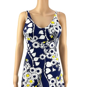 Puede incluir: Vestido azul marino sin mangas con estampado floral blanco y amarillo. El vestido presenta un escote en V y un corpiño ajustado, con una falda fluida. El diseño floral incluye margaritas y formas de hojas.