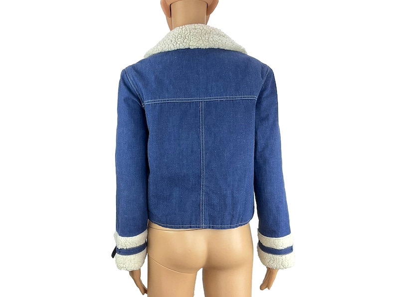 K&ouml;nnte beinhalten: Blaue Jeansjacke mit wei&szlig;em Kunstfellkragen und -b&uuml;ndchen. Die Jacke hat ein klassisches Design mit Knopfverschluss und eine verk&uuml;rzte Passform. Die Manschetten haben eine wei&szlig;e Kunstfellverbr&auml;mung.