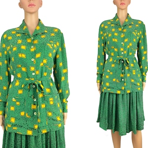 May include: A green and yellow patterned dress with a long-sleeved shirt and a skirt. The shirt has a button-up front and a belt. The skirt is pleated.