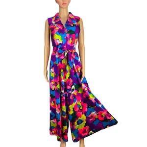 May include: A sleeveless jumpsuit featuring a vibrant, multicolored floral pattern in shades of bright pink, purple, blue, and green. The garment has a collared neckline, a button-down front, and a matching fabric tie belt at the waist.