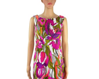 May include: Sleeveless dress with a vibrant floral print featuring large pink, purple, and white flowers on a white background. The dress has a scoop neckline and a fitted waist, creating a flattering silhouette. The floral pattern includes green and orange accents.