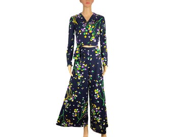 May include: A two-piece navy blue outfit featuring a wrap top and wide-leg pants. The ensemble is adorned with a floral pattern in shades of yellow, green, and purple. The top has long sleeves and a tie closure at the waist.
