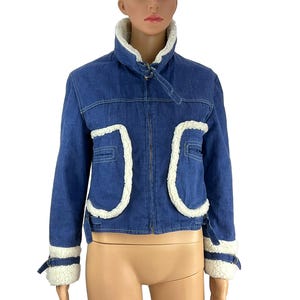K&ouml;nnte beinhalten: Blaue Jeansjacke mit wei&szlig;em Kunstfellbesatz. Die Jacke hat einen hohen Kragen, Vordertaschen und Manschetten mit wei&szlig;em Besatz. Ein klassischer Stil f&uuml;r verschiedene Anl&auml;sse.
