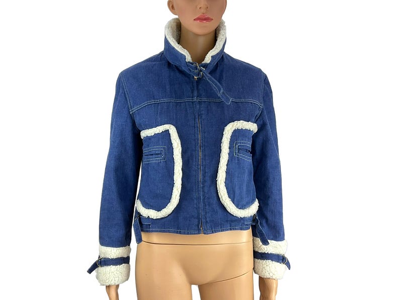K&ouml;nnte beinhalten: Blaue Jeansjacke mit wei&szlig;em Kunstfellbesatz. Die Jacke hat einen hohen Kragen, Vordertaschen und Manschetten mit wei&szlig;em Besatz. Ein klassischer Stil f&uuml;r verschiedene Anl&auml;sse.