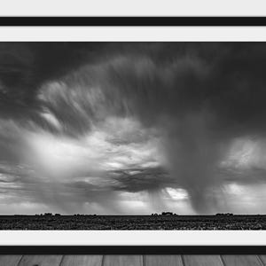 May include: A black and white photograph of a dramatic sky with dark, swirling clouds and a field in the foreground.