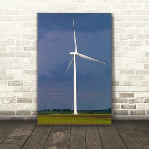 May include: A white wind turbine with three blades against a blue sky with clouds. The turbine is in a field of green grass.