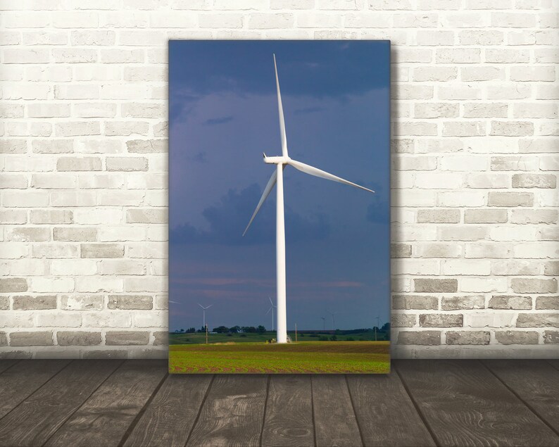 May include: A white wind turbine with three blades against a blue sky with clouds. The turbine is in a field of green grass.