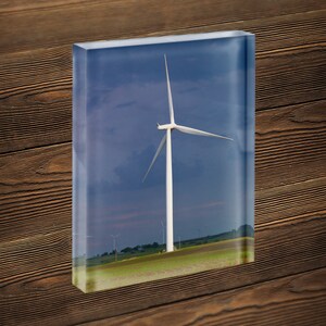 May include: A white wind turbine with three blades stands tall in a field of green grass against a blue sky with white clouds.