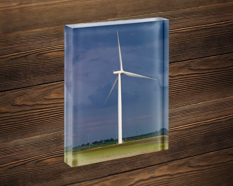 May include: A white wind turbine with three blades stands tall in a field of green grass against a blue sky with white clouds.