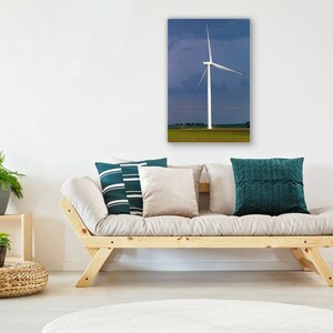 May include: A white wind turbine with three blades stands tall against a blue and purple sky. The turbine is in a field of green grass. The image is a photograph of a canvas print.