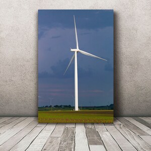 May include: A white wind turbine with three blades against a blue sky with clouds. The turbine is in a field of green grass.