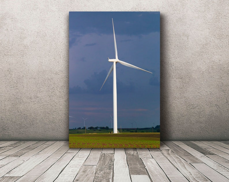 May include: A white wind turbine with three blades against a blue sky with clouds. The turbine is in a field of green grass.