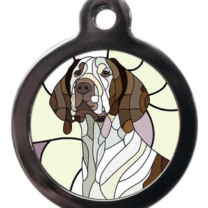 May include: A round, silver dog tag featuring a stained glass image of a brown and white German Shorthaired Pointer dog. The dog is looking to the left and has a light yellow background.