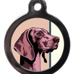 May include: A round silver dog tag featuring a pink and black illustration of a German Shorthaired Pointer dog's head. The dog is looking to the right.
