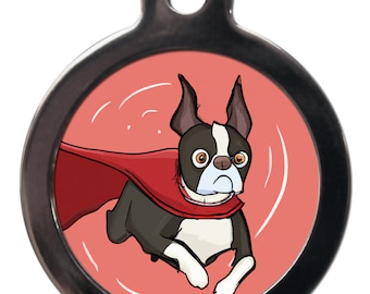 Peut inclure: Une médaille ronde en argent avec un fond rouge et une image de dessin animé d'un Boston Terrier noir et blanc portant une cape rouge et volant. Le chien a une expression sérieuse sur son visage.