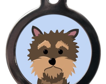 Puede incluir: Una chapa redonda de perro de plata con una ilustración de un perro Yorkshire Terrier marrón y tostado sobre un fondo azul claro.