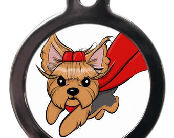 Puede incluir: Una chapa redonda de perro de plata con fondo blanco y una imagen de dibujos animados de un Yorkshire Terrier con una capa roja y un lazo rojo. El perro corre con la lengua fuera.
