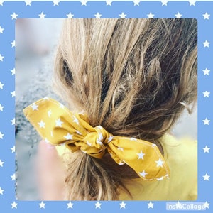 Puede incluir: Una liga para el pelo amarilla con estrellas blancas. La liga está atada alrededor de una coleta.