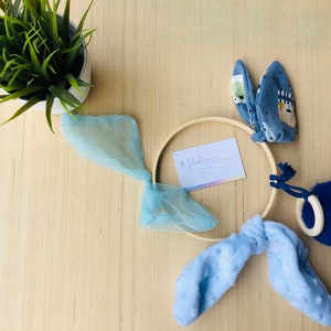 May include: A blue and white baby mobile with a wooden ring, blue fabric, and a blue pom-pom. The mobile is hanging from a wooden hoop.
