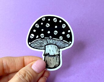 May include: A black and white sticker of a mushroom with a black cap covered in white skulls. The mushroom has a white stem with a brown base.