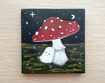 May include: A small painting of a red and white mushroom with white spots, with a white ghost sitting under it. The background is a dark blue with white stars and a crescent moon.