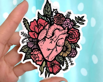 May include: A sticker featuring a stylized anatomical heart surrounded by pink, red, and yellow flowers. The heart is a light pink color and the flowers are outlined in black.