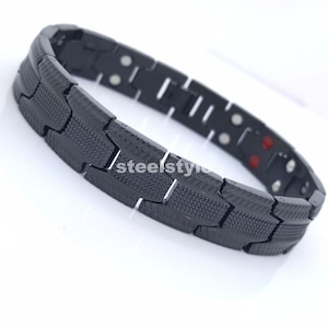 May include: A black magnetic bracelet with a textured design. The bracelet is made of metal and has a clasp closure.