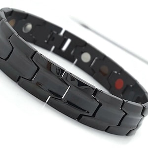 May include: A black magnetic bracelet with a textured, interlocking design. The bracelet has multiple small, round magnets embedded in the links.