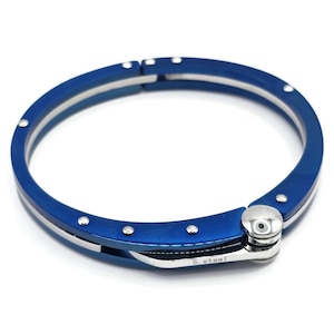 Może przedstawiać: Bransoletka typu bangle ze stali nierdzewnej w kolorze niebieskim z zapięciem na zawias. Bransoletka ma polerowane wykończenie i jest ozdobiona małymi srebrnymi kropkami.