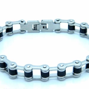 May include: A silver-coloured bracelet with a bicycle chain design. The bracelet features alternating silver links and black rubber inserts, secured with a clasp. This accessory is a unique piece of jewellery.