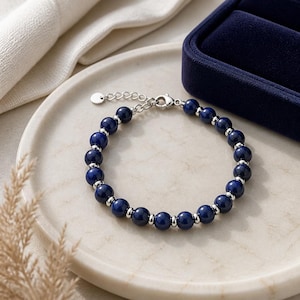 Puede incluir: Una pulsera de cuentas con piedras redondas de lapislázuli azul intenso que se alternan con pequeños espaciadores de metal plateado pulido. La pulsera incluye un cierre de mosquetón plateado, una cadena de extensión ajustable y un pequeño dije redondo.
