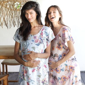 May include: Two people wearing floral print maternity dresses. The dress on the left is light blue with a floral pattern and the text "Hillary" embroidered on the front. The dress on the right is peach with a floral pattern and the text "Kerri" embroidered on the front.