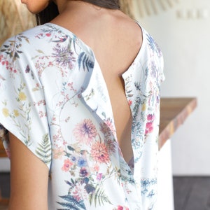 May include: A white, floral print nursing top with a button-up opening at the back. The top has short sleeves and a relaxed fit.