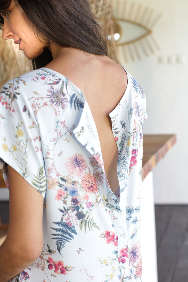 May include: A white, floral print nursing top with a button-up opening at the back. The top has short sleeves and a relaxed fit.